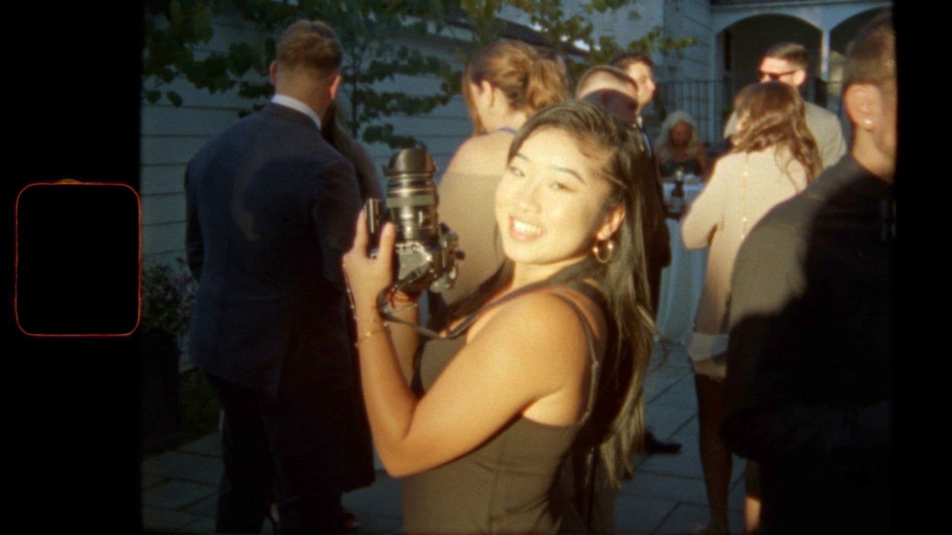 A smiling videographer with a professional camera at an outdoor wedding reception, captured in a warm, cinematic style.
